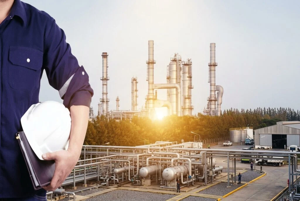 Engineer holding a safety helmet in front of an industrial plant