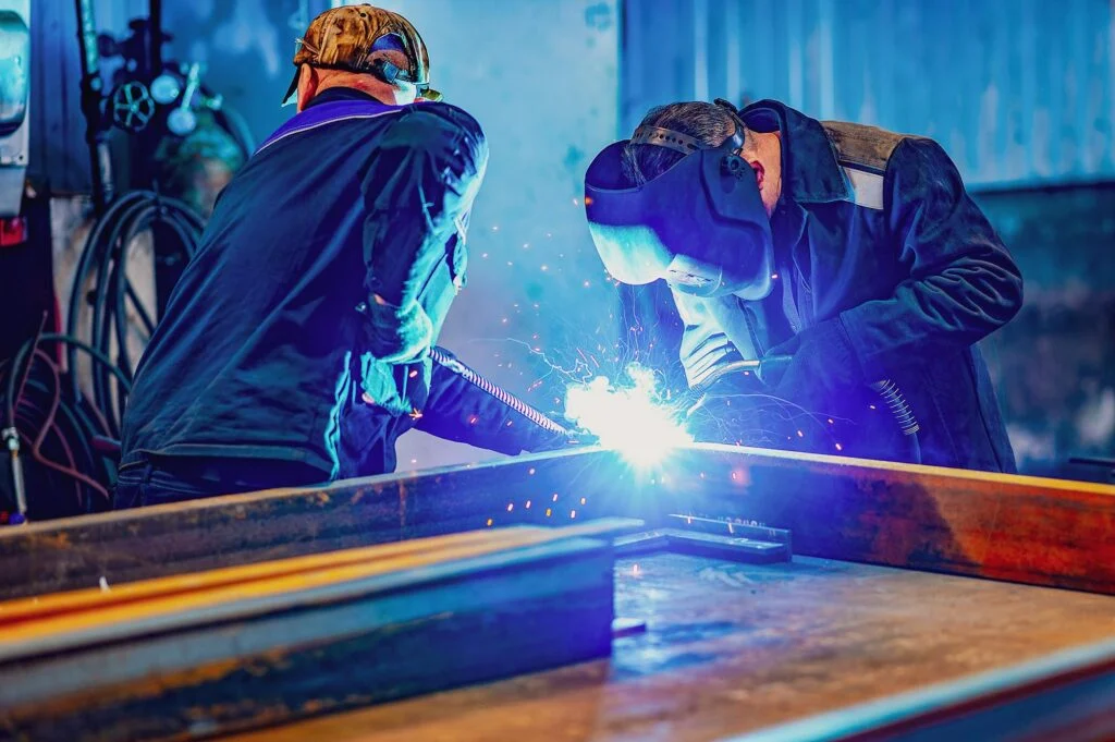 Two welders in protective masks fabricating structural steel
